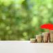Des pièces de monnaie abritées sous un parapluie rouge miniature