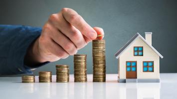 Des piles de pièces de monnaie posées à côté d'une maison miniature