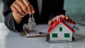 Une femme qui tient des clés à côté d'une maison miniature colorée posée sur un bureau