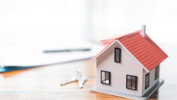 Une maison miniature posée sur un bureau avec des clés et des papiers