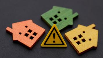 Trois maisons miniatures avec signe d'avertissement d'exclamation concept de risque et de danger pour l'immobilier