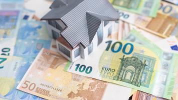 Une maison miniature posée sur des billets de banque en euros