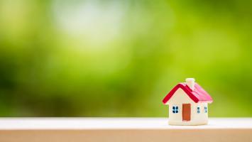 Une maison miniature au toit rouge avec en arrière-plan un fond vert