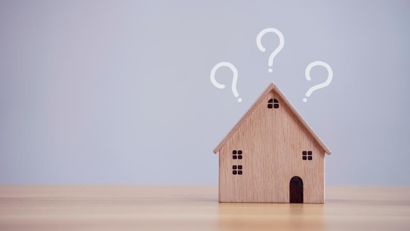 Des points d'interrogation au-dessus d'une maison miniature en bois clair