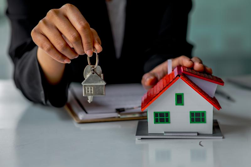 Une femme qui tient des clés à côté d'une maison miniature colorée posée sur un bureau