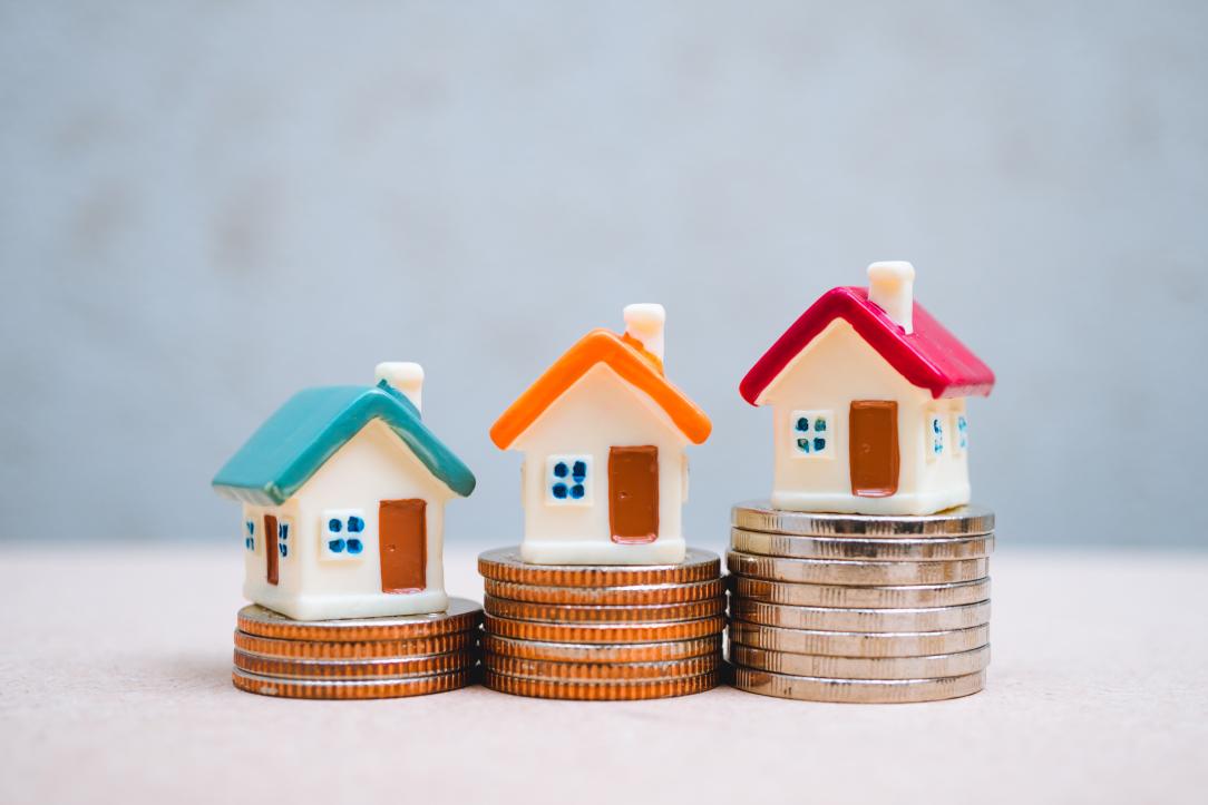 Des maisons miniatures colorées posées sur des piles de pièces de monnaie