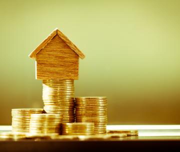 Une maison miniature en bois posée sur une pile de pièces de monnaie dorées
