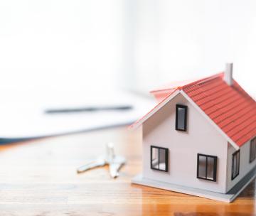 Une maison miniature posée sur un bureau avec des clés et des papiers