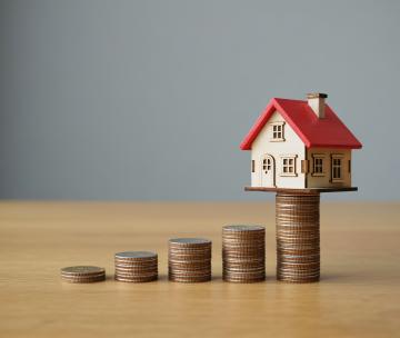 Une maison miniature posée en équilibre sur des pièces de monnaie
